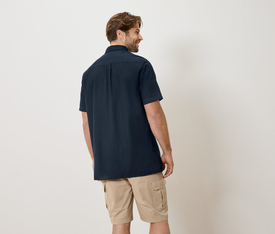 Mann von hinten in marineblauem Hemd und beigen Shorts.