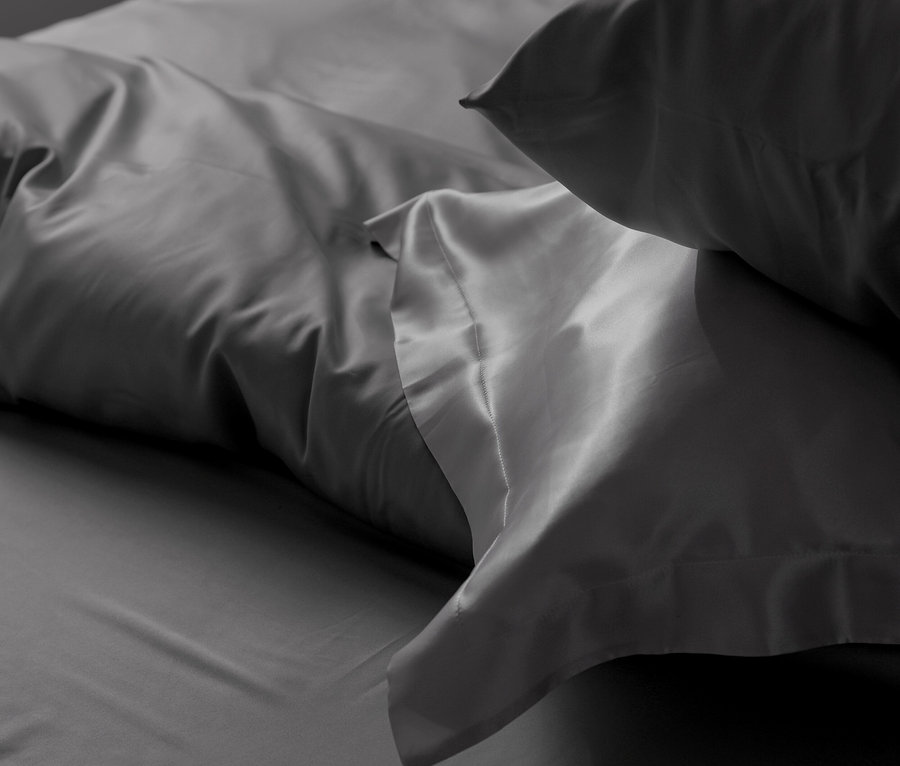 Nahaufnahme von grauer Bettwäsche mit Kissen und Laken.