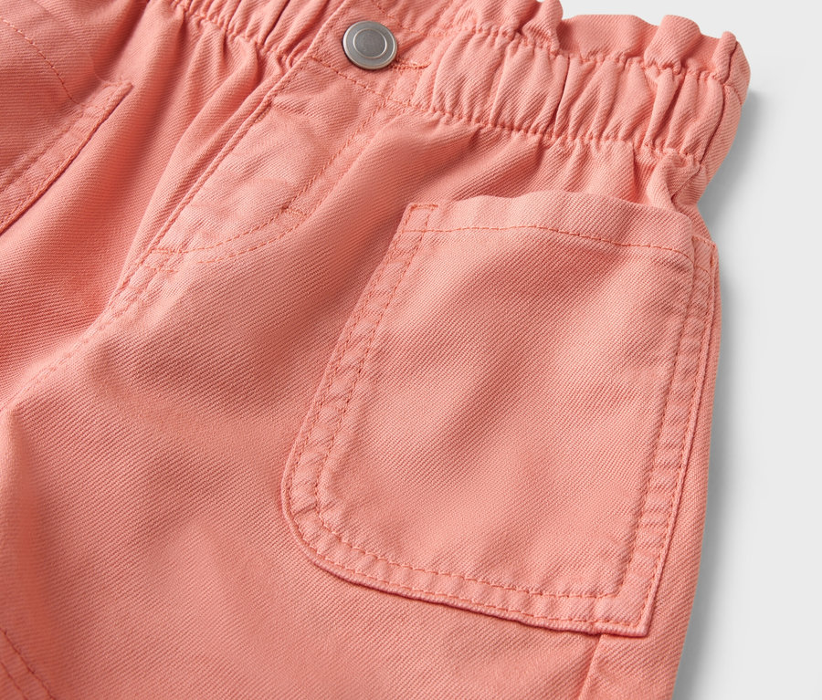 Nahaufnahme einer lachsfarbenen Shorts mit Gummibund und aufgesetzter Tasche.