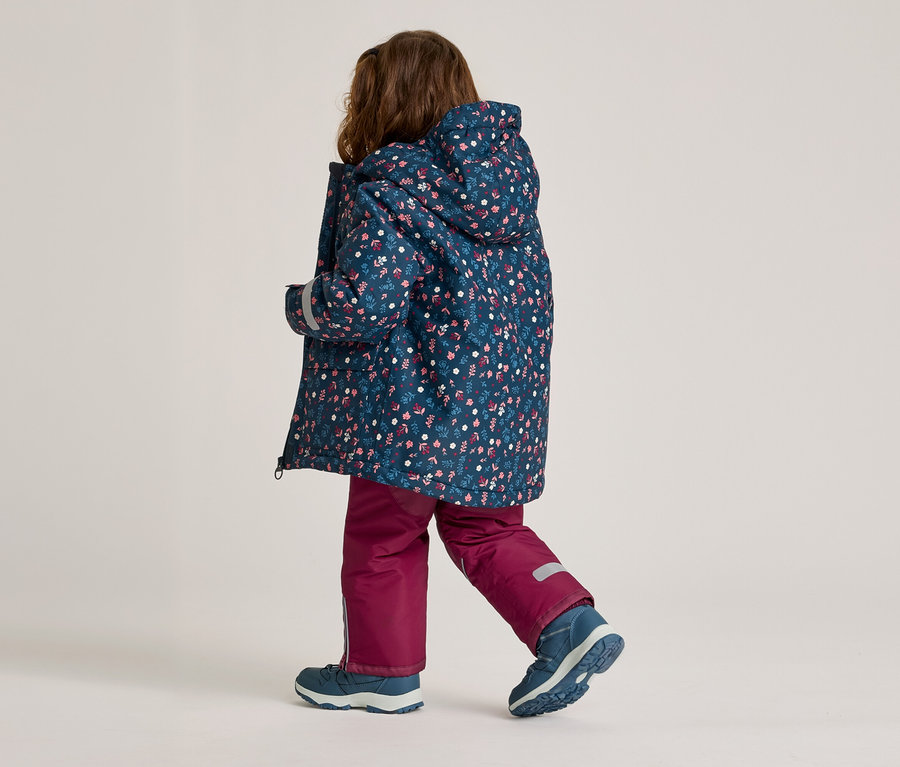 Kind von hinten in floral gemusterter Jacke mit Kapuze, weinroter Hose und blauen Schuhen.