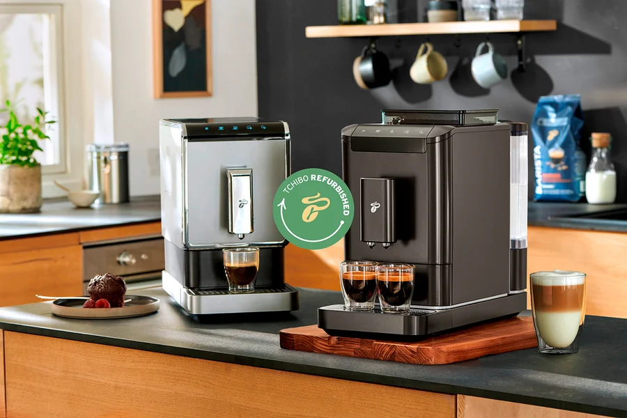Zwei Kaffeemaschinen stehen auf einer Küchentheke, eine silberne und eine dunkle, jeweils mit Tassen Kaffee davor.