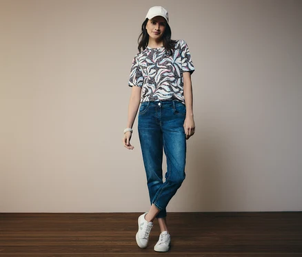 Frau in blauem CECIL Kurzarmshirt und CECIL Jeans »Scarlett«, dazu weiße Schuhe und Kappe.
