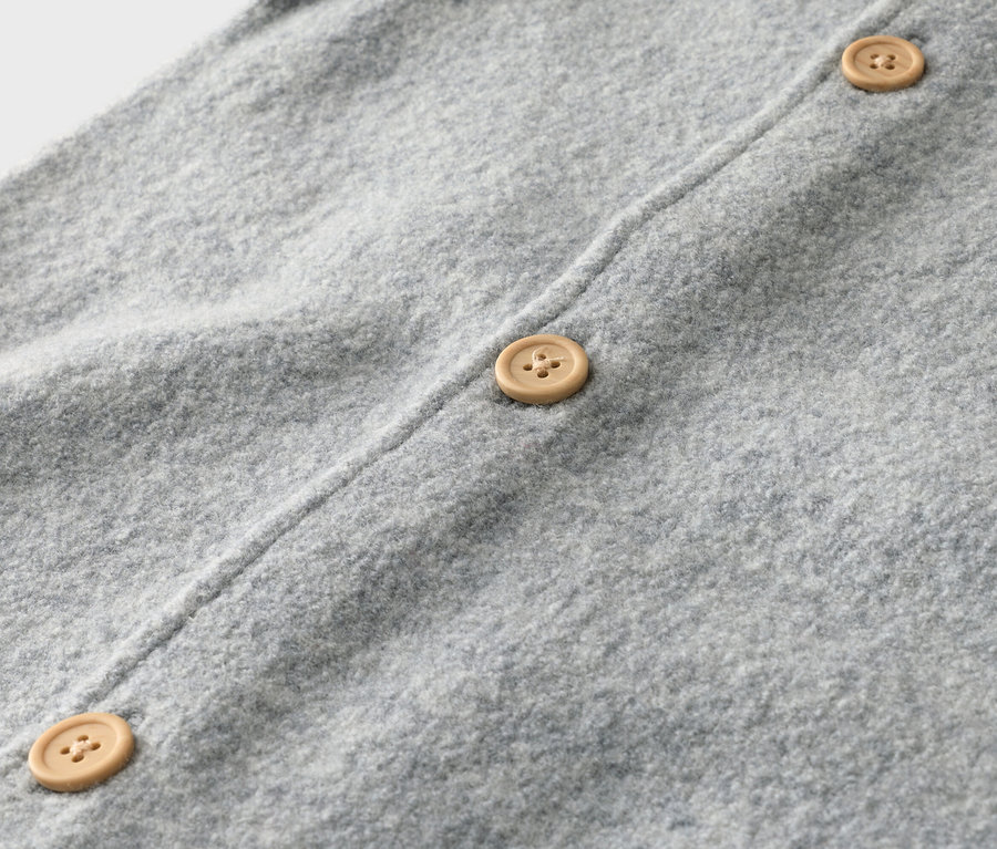 Nahaufnahme eines hellgrauen Strickcardigans mit drei hellbraunen Knöpfen.