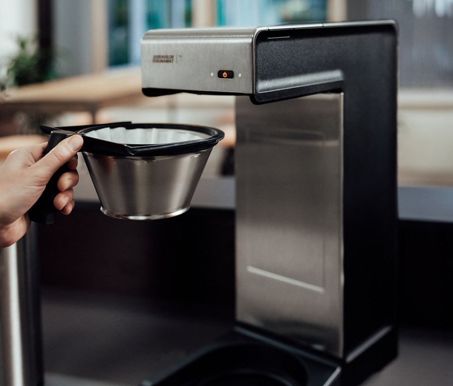 Hand hält Filter in Kaffeemaschine.
