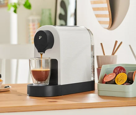 Cafissimo pure+, white Kaffeemaschine füllt Kaffee in ein Glas. Im Hintergrund befindet sich ein Muffin.