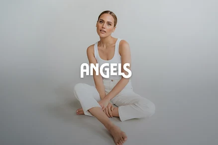 Frau sitzt auf dem Boden, trägt ein weißes Tanktop und eine weiße Hose, die Beine sind gekreuzt, blickt in die Kamera. Überlagert mit dem Text „ANGELS“.