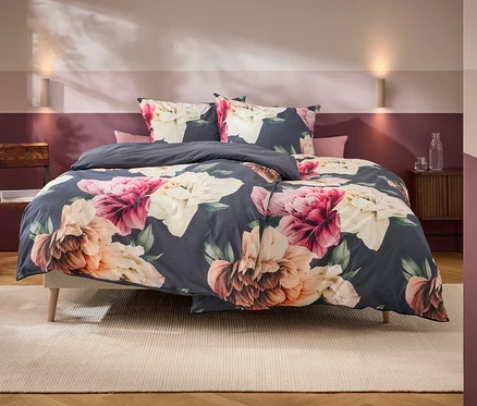 Ein Bett mit dunkelgrauer Bettwäsche und großen rosa, weißen und orangefarbenen Blumenmustern steht in einem Schlafzimmer mit zweifarbiger Wand und Holzmöbeln.