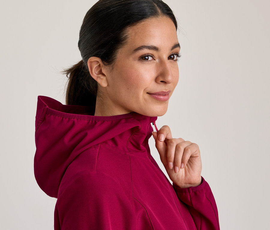 Frau in einer magentafarbenen Kapuzenjacke, die sie zuzieht und über die Schulter blickt.