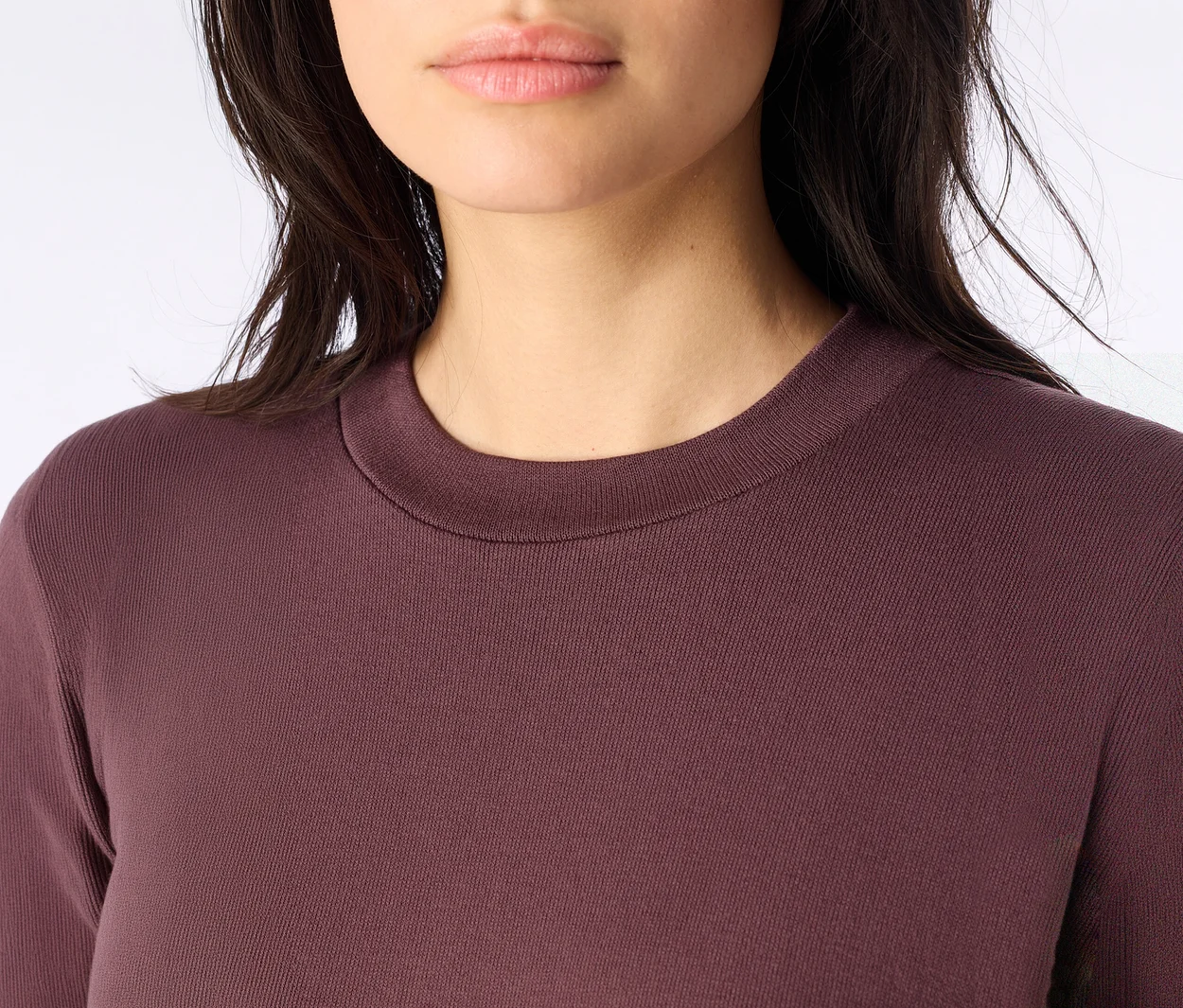 Nahaufnahme einer Frau, die ein dunkelrotes Langarmshirt mit Rundhalsausschnitt trägt, wobei ihr Kinn und Hals sichtbar sind. Ihr dunkles Haar ist zu sehen.