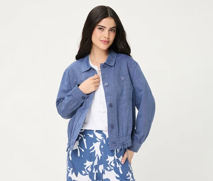 Eine Frau trägt eine blaue Olsen Jeansjacke über einem weißen Oberteil und einem blau-weiß gemusterten Rock.