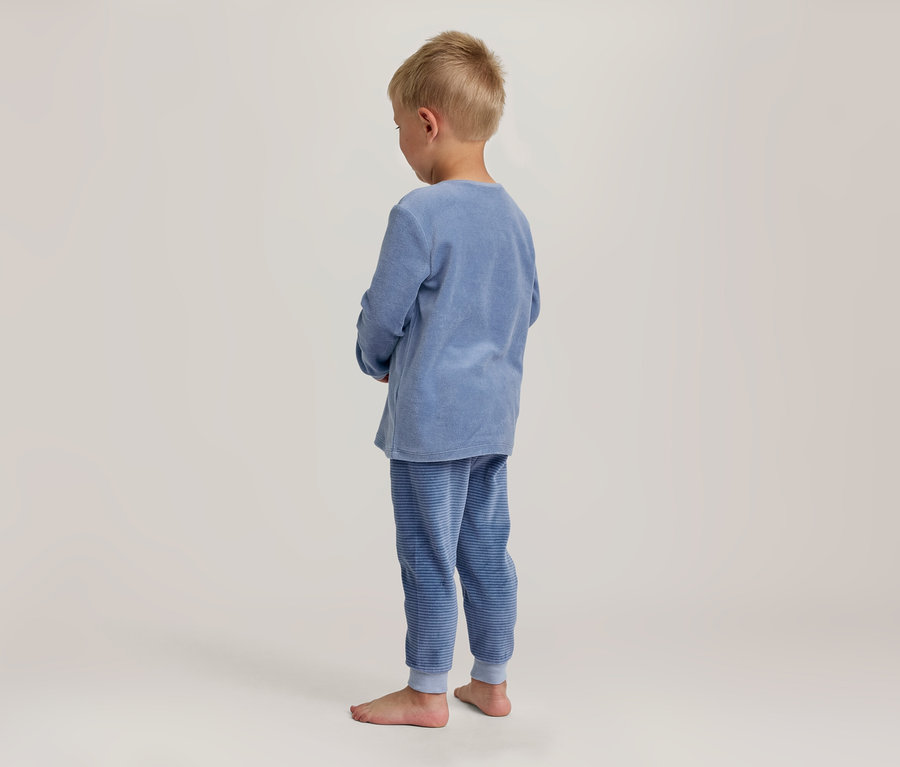 Junger Junge von hinten, trägt blaues Langarmshirt und blau gestreifte Pyjamahose, blickt nach unten. Er ist barfuß.