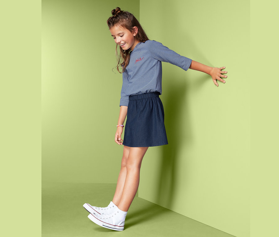 Mädchen posiert im Kleid im Materialmix an einer Wand.