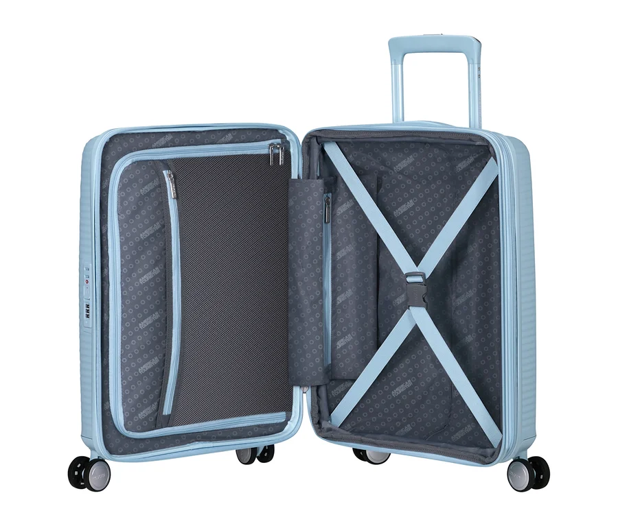Offener American Tourister Soundbox Hartschalen-Koffer in Pastellblau, der seine beiden Hälften zeigt. Die linke Hälfte hat eine Reißverschluss-Netztrennwand, die rechte elastische Kreuzgurte und einen Teleskopgriff.