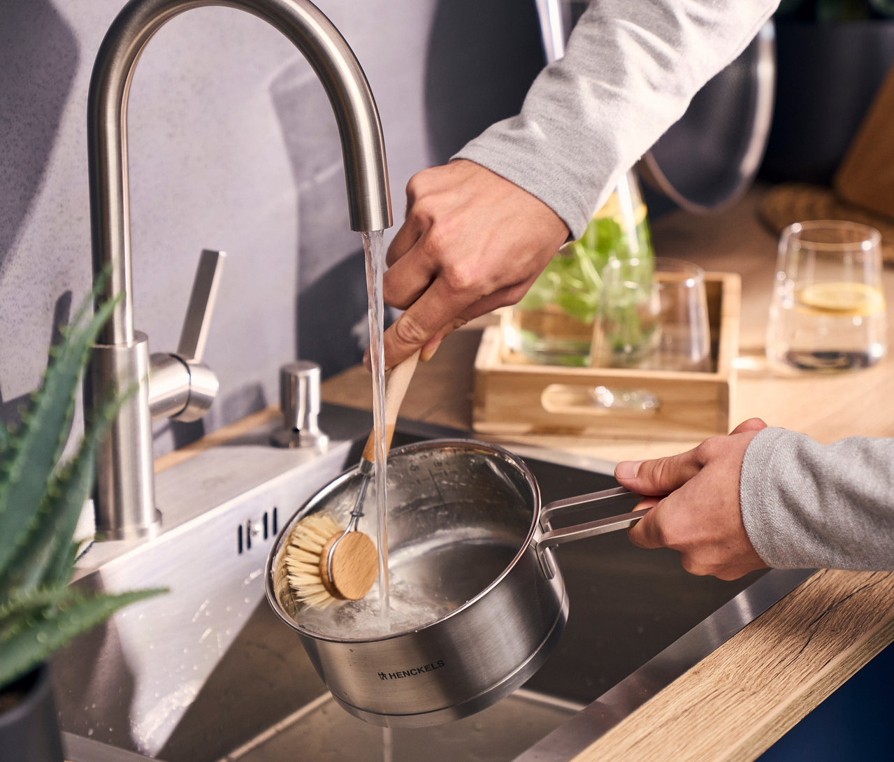 Hände waschen einen silbernen Henckels Topf aus dem Henckels by ZWILLING »Pulse« Kochgeschirrset, 5-teilig, mit Bürste im Spülbecken.