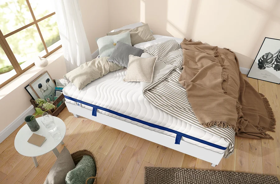 Weißes Bettgestell mit Matratze, Kissen und beige Decke im Schlafzimmer.