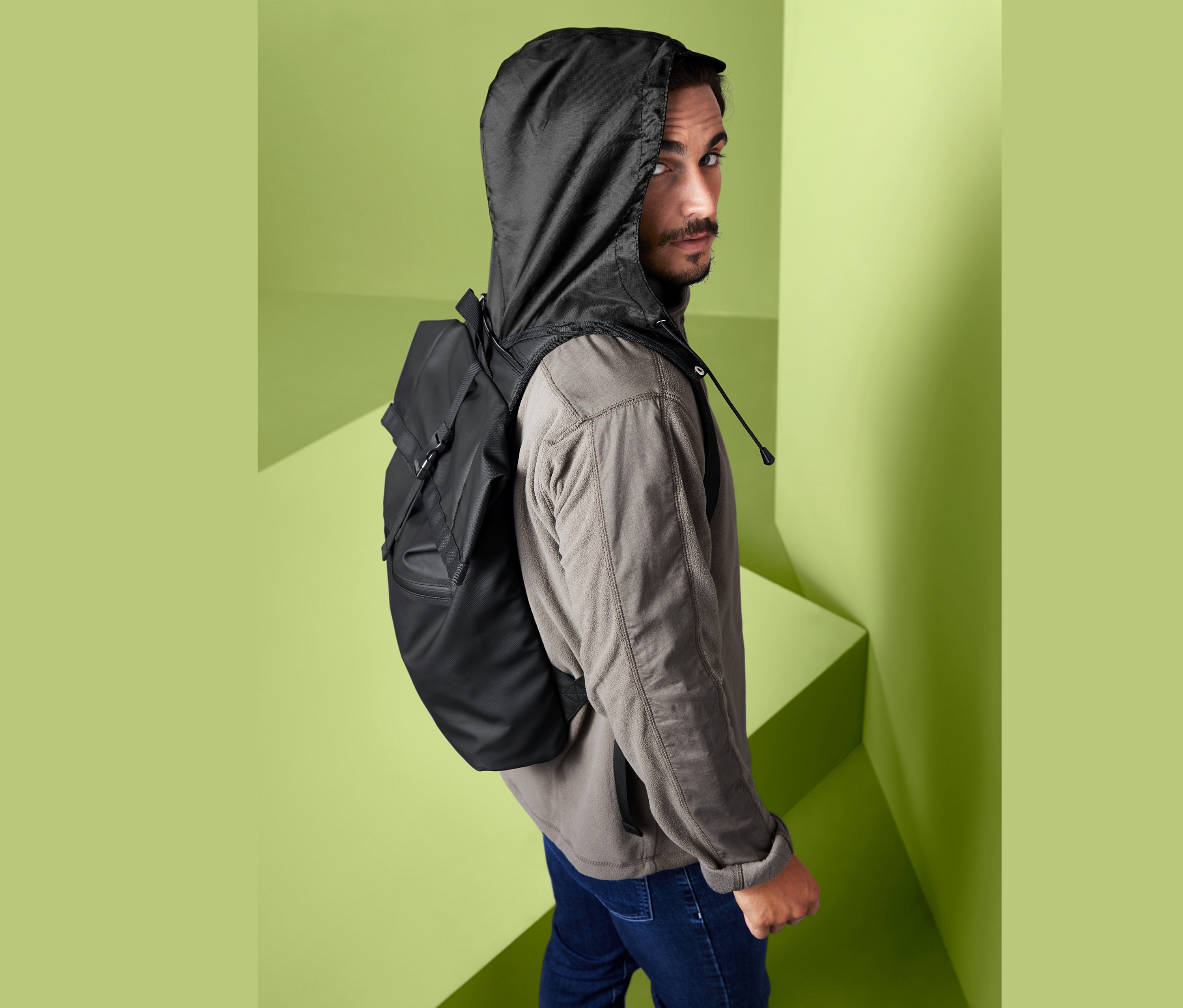 Mann blickt über die Schulter und trägt einen urbanen Rucksack mit Kapuze.