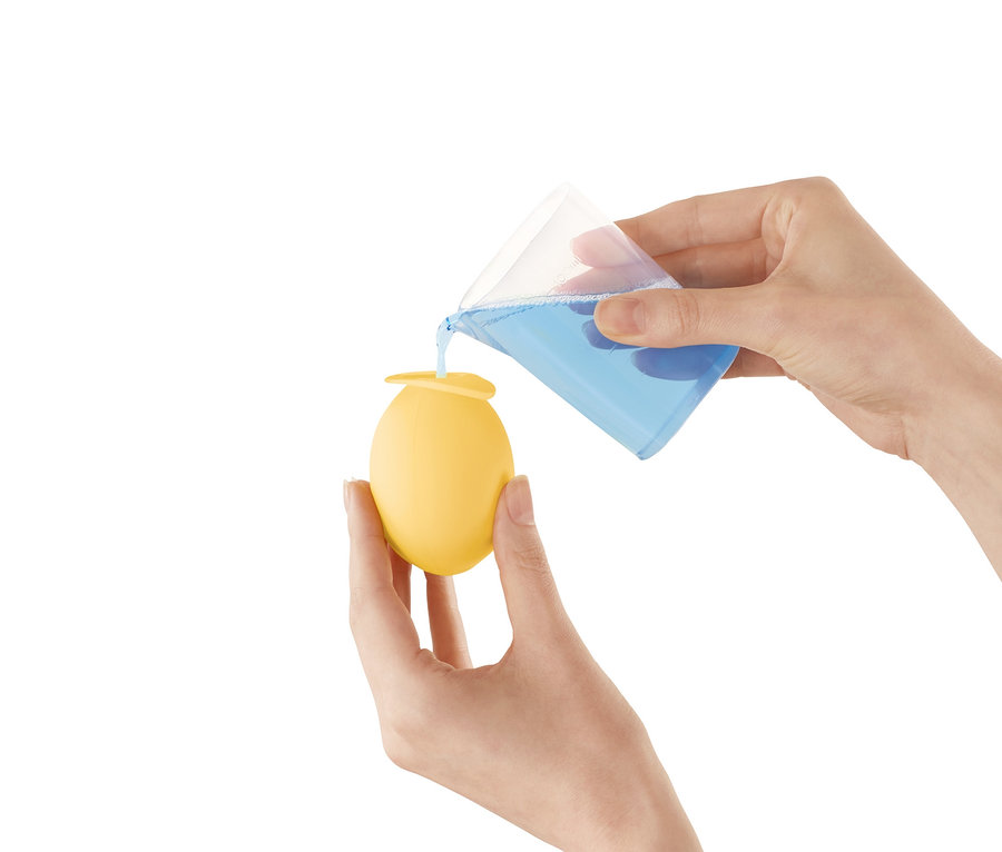 Frau gießt blaue Flüssigkeit aus einem Messbecher in einen gelben Wasserhahn-Entkalker-Aufsatz.