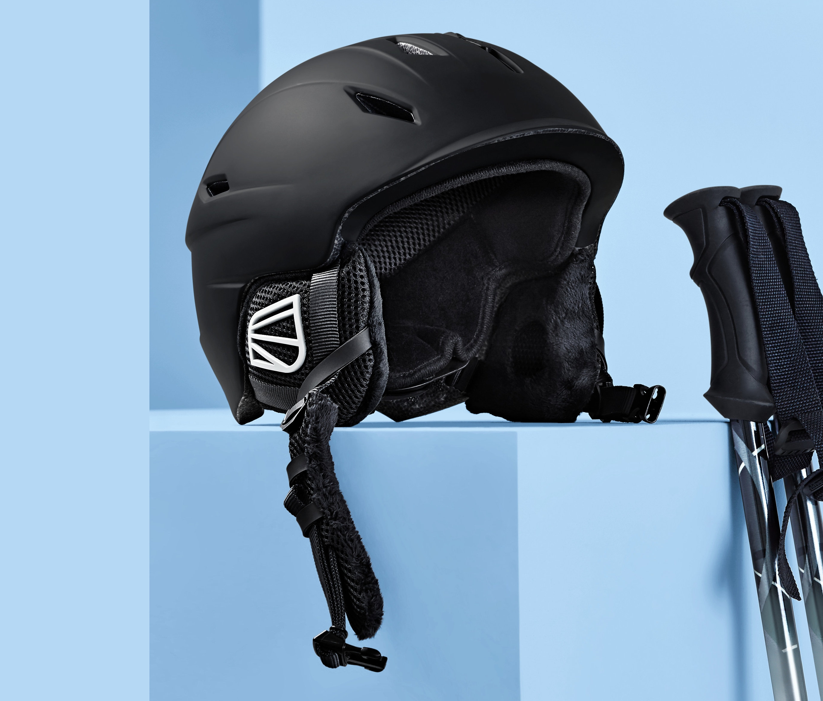 Schwarzer In-Mould-Ski- und Snowboardhelm und Skistöcke auf blauem Hintergrund.