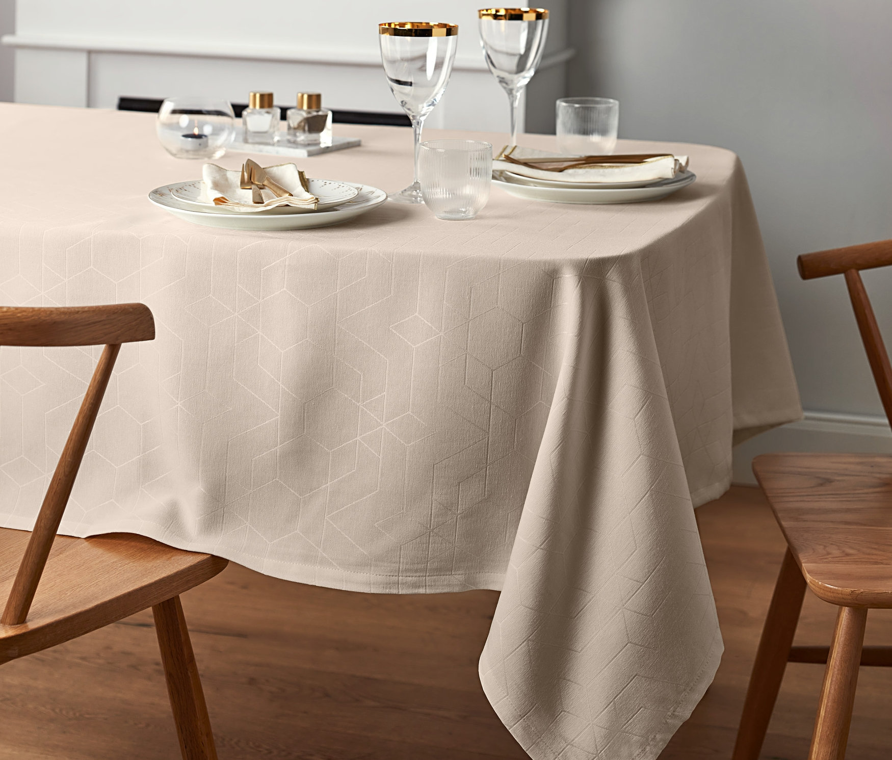 Gedeckter Tisch mit einer cremefarbenen Jacquard-Tischdecke in Normalgröße, Tellern, Gläsern und Holzstühlen.