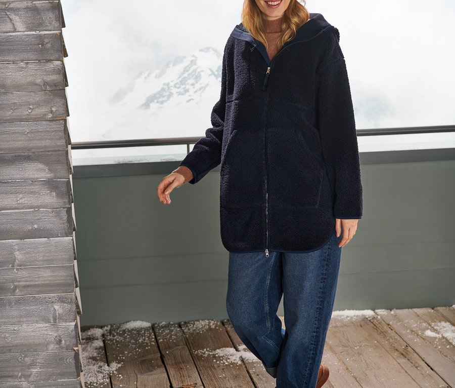 Frau trägt einen Oversized Teddymantel, Jeans und eine Mütze.