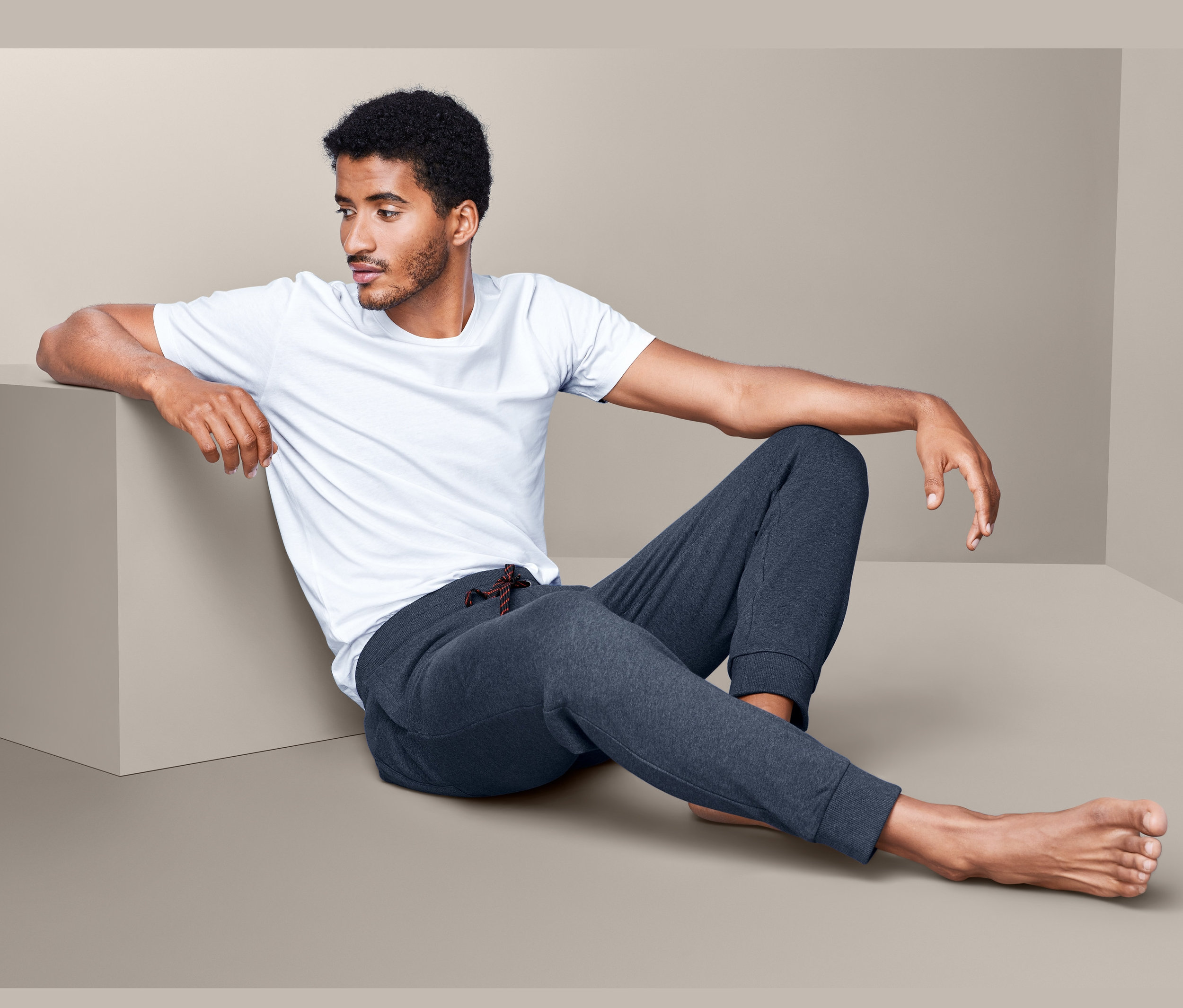 Mann sitzt und trägt eine Homewearhose und ein weißes T-Shirt.