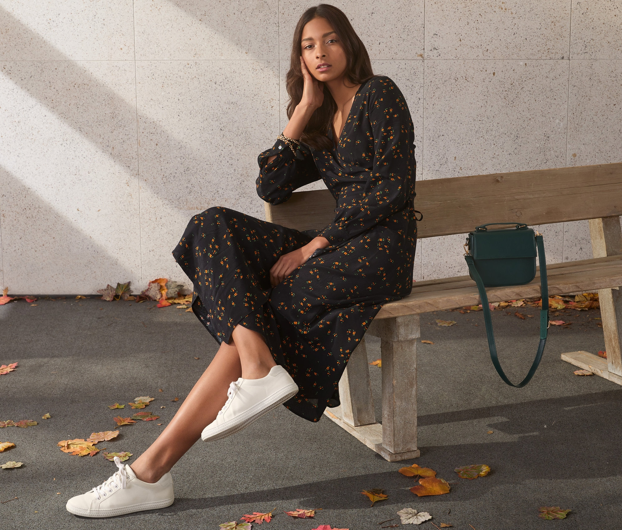 Eine Frau sitzt in einem Wickelkleid und weißen Turnschuhen auf einer Bank.