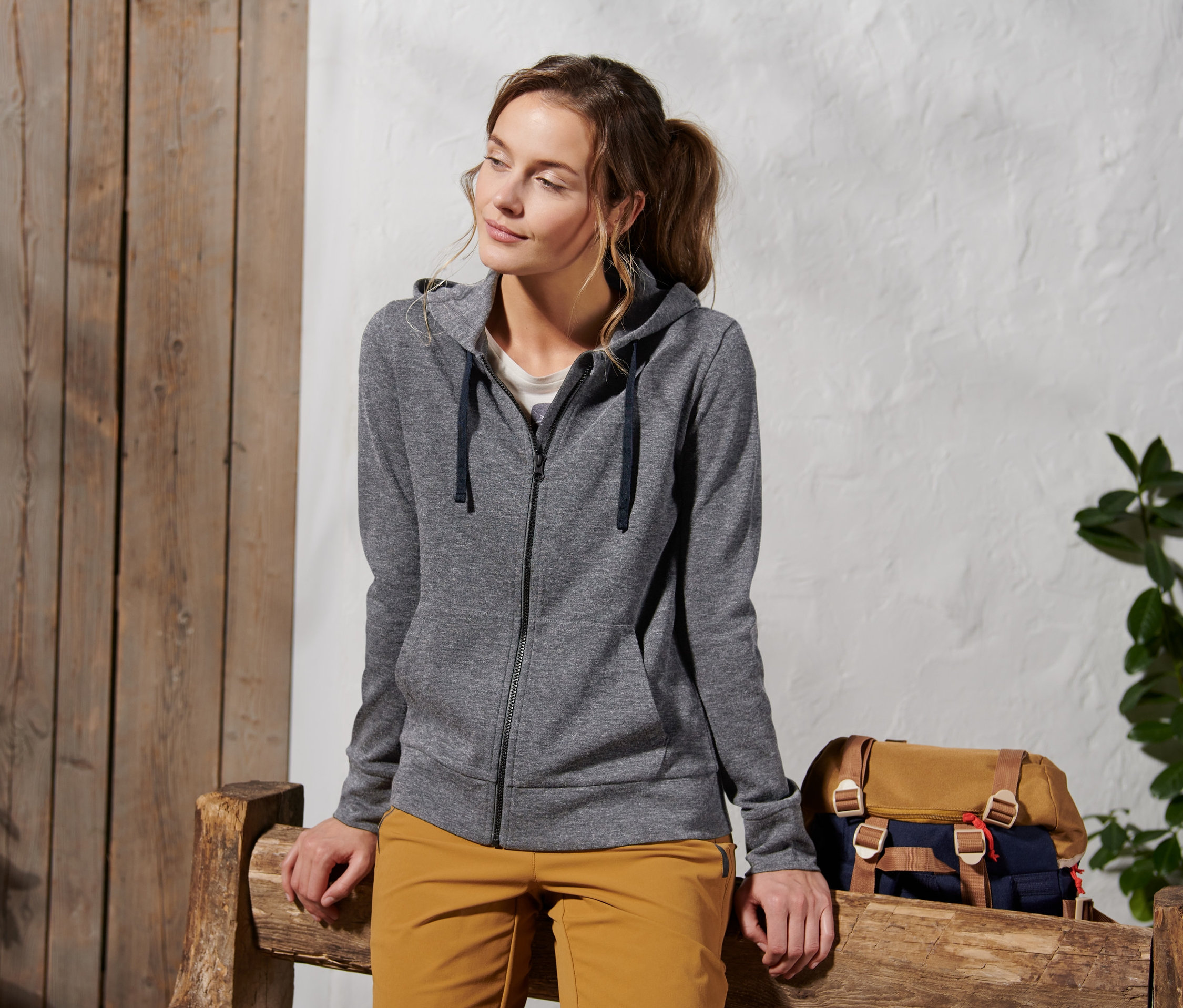 Frau sitzt auf Holzbank und trägt eine Kapuzenjacke mit RWS-zertifizierter Wolle, grau.