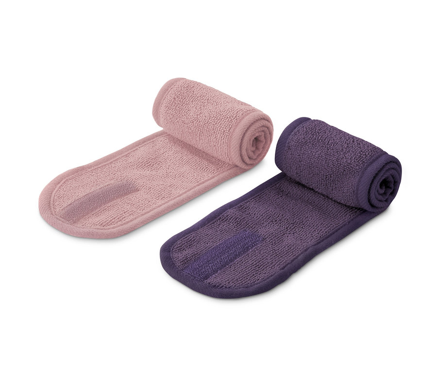 Zwei Kosmetik-Stirnbänder, eines rosa und eines lila, liegen nebeneinander auf einem weißen Hintergrund.