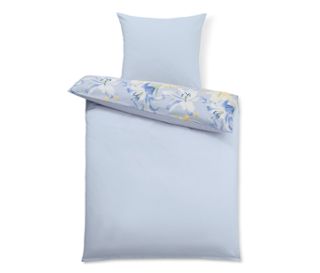 Hellblaue Bettwäsche mit floralem Kissen.