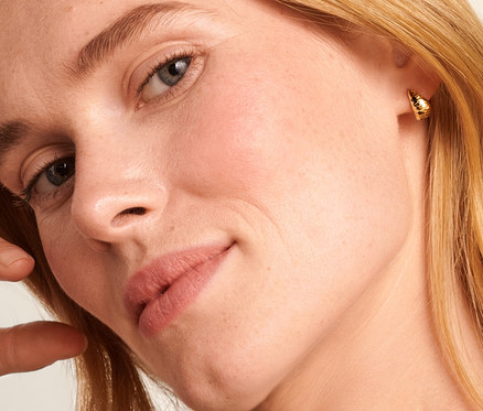 Blonde Frau mit Hand am Kopf trägt eine 585 Gold Kette Singapur und 375 Gold Halbcreolen konisch diamantiert.
