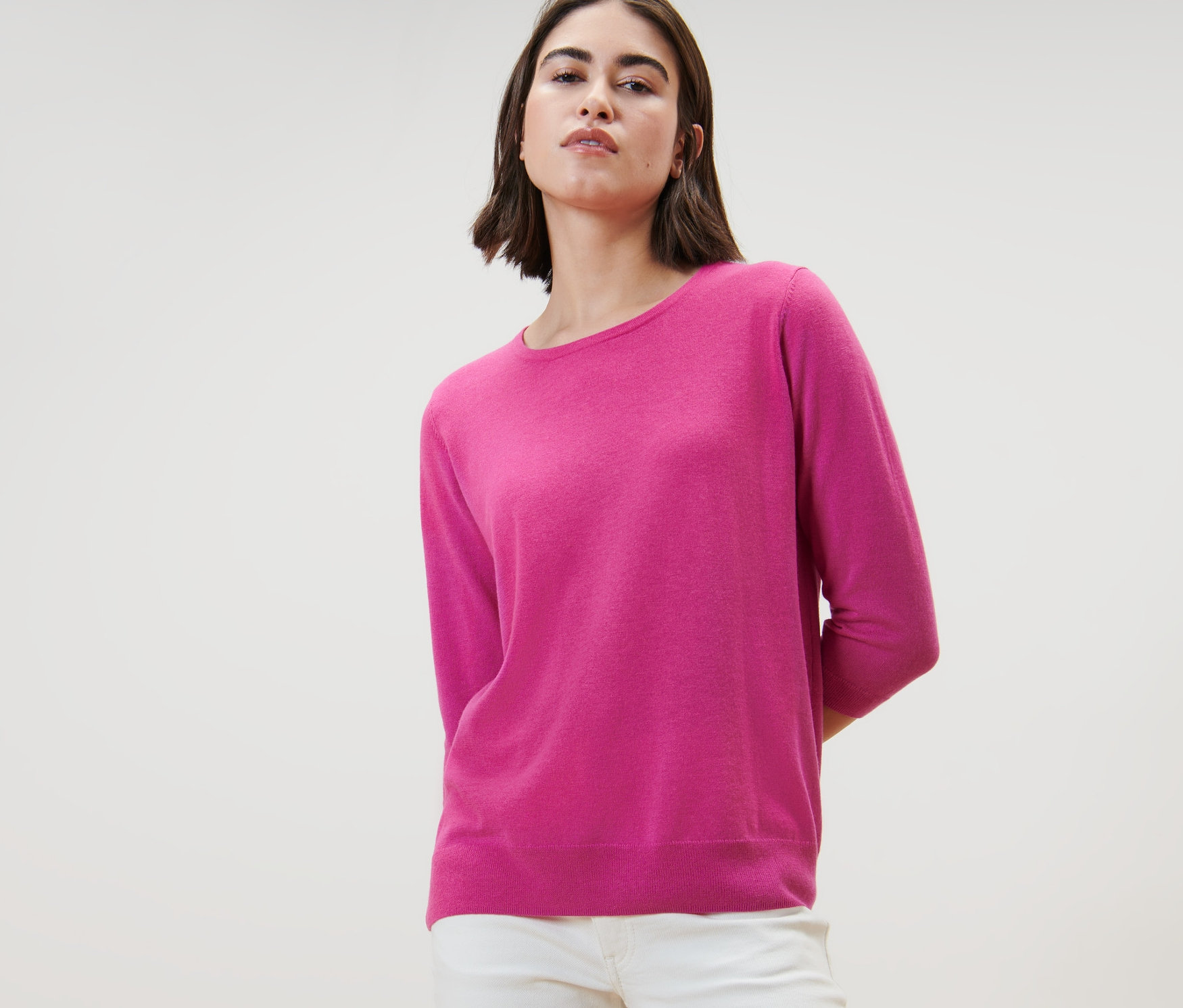 Frau trägt einen pinken Feinstrickpullover mit Seide und eine weiße Hose.