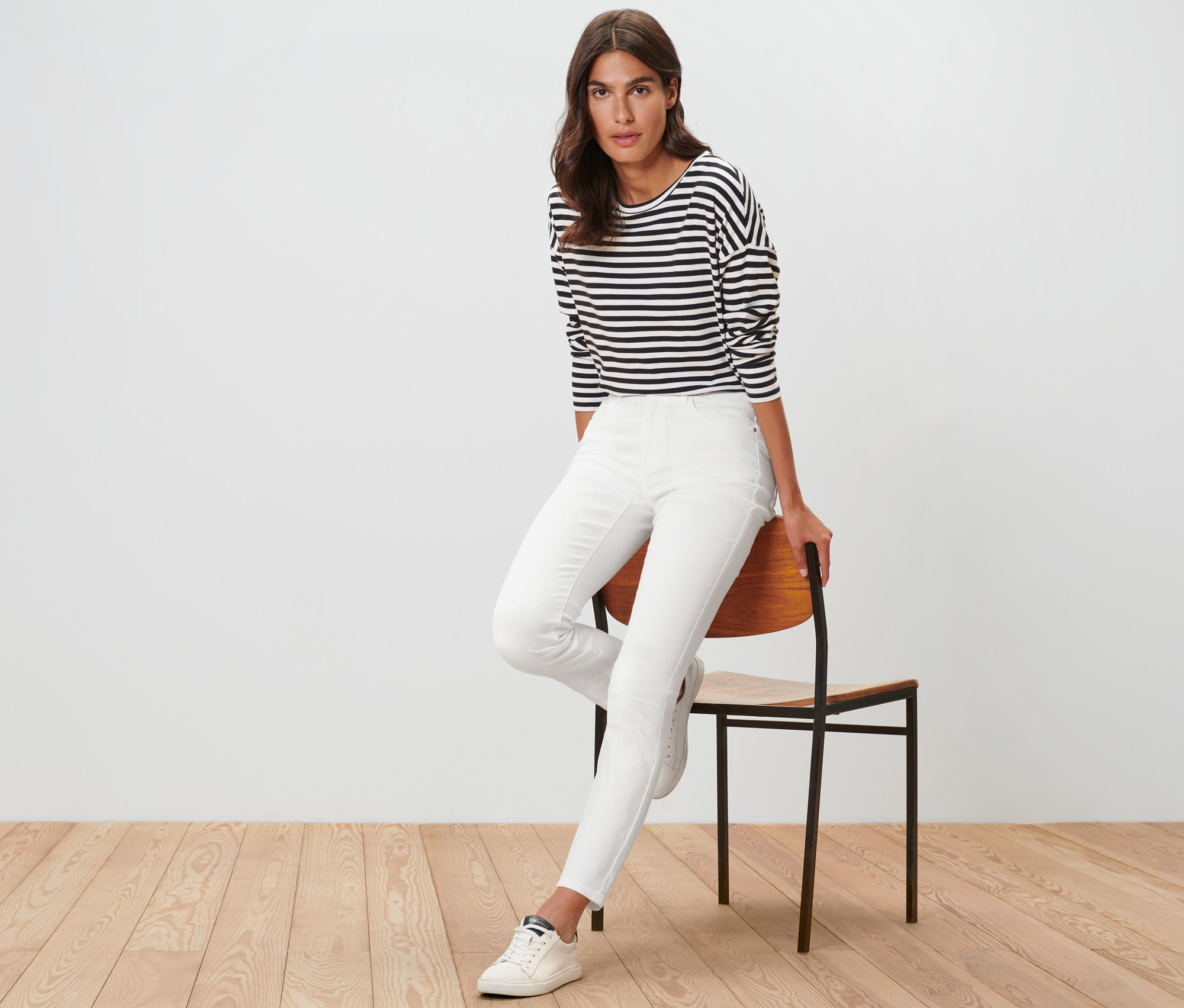 Frau sitzt auf einem Stuhl und trägt eine cremefarbene Colored Jeans – Fit »Emma«.