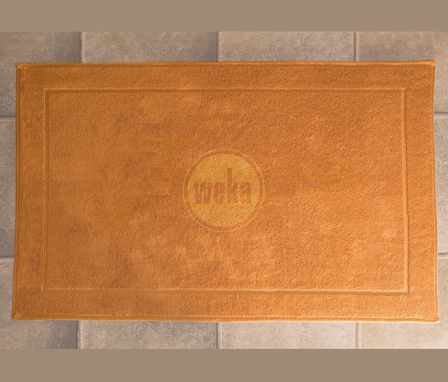 Draufsicht auf eine orangefarbene Badematte mit Weka-Logo auf grauem Fliesenboden.