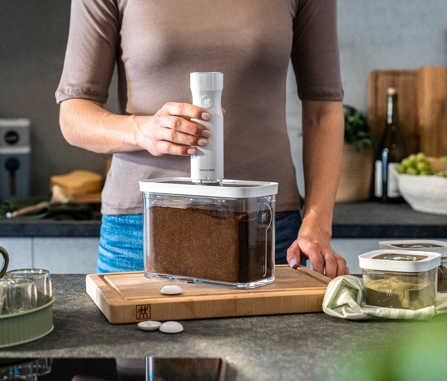 Eine Frau verwendet ein ZWILLING FRESH & SAVE CUBE Starter-Set M, um in der Küche Kaffee zu vakuumieren.