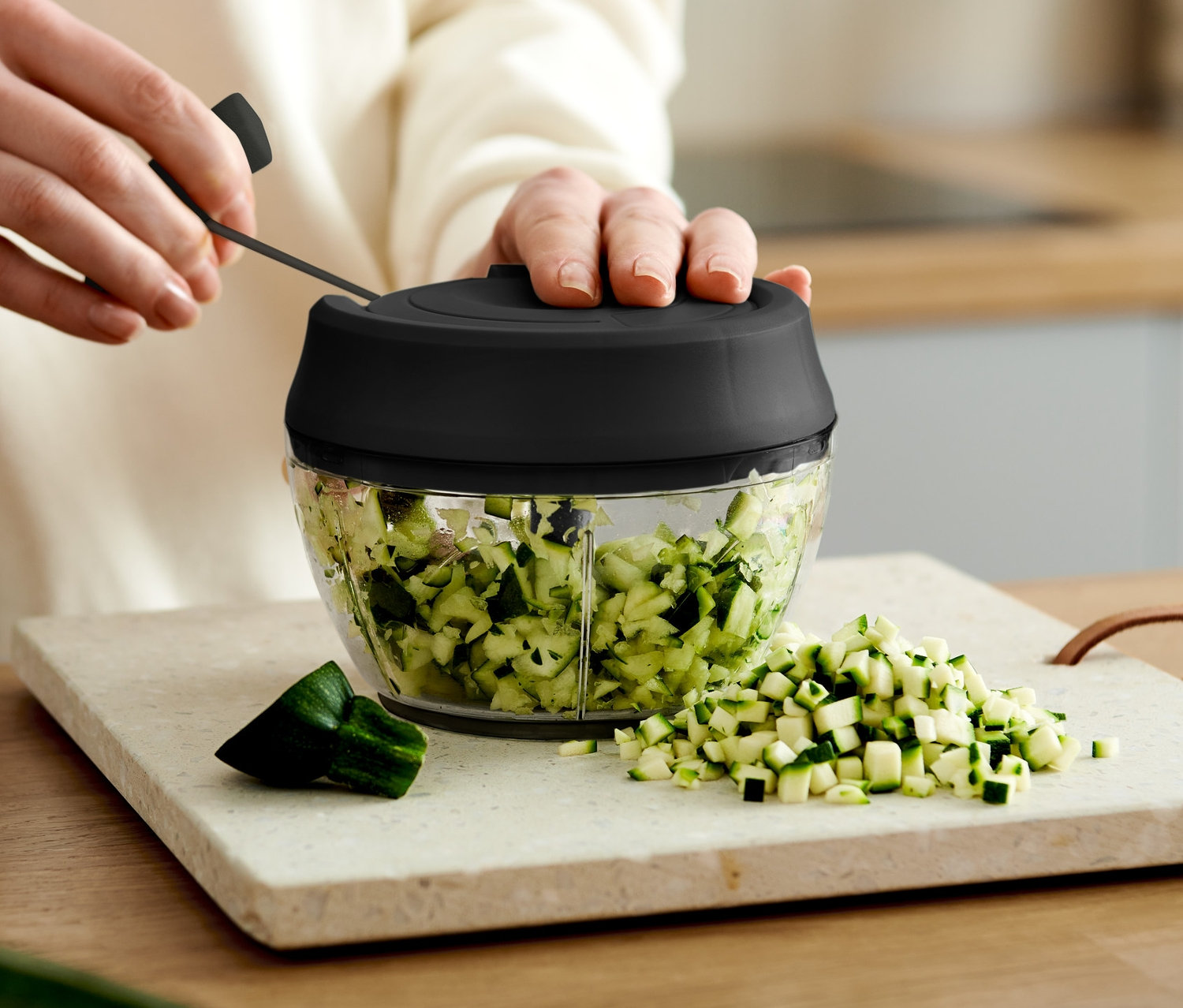 Eine Person benutzt einen manuellen Multizerkleinerer, um Zucchini in Würfel zu schneiden.