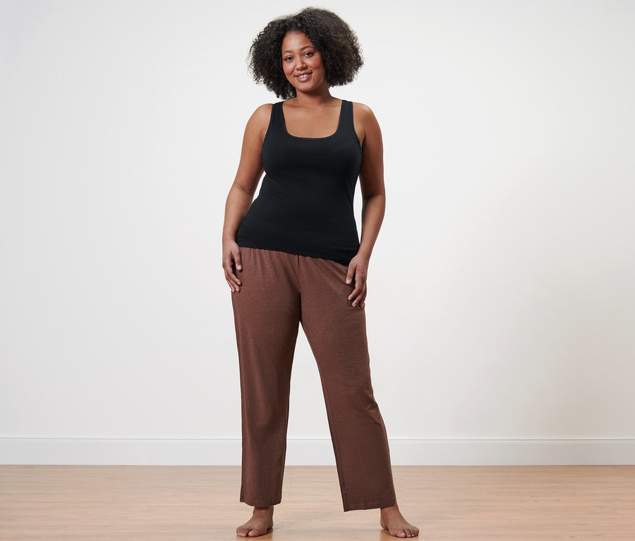 Frau steht barfuß in Pyjamahose und einem schwarzen Hemdchen.