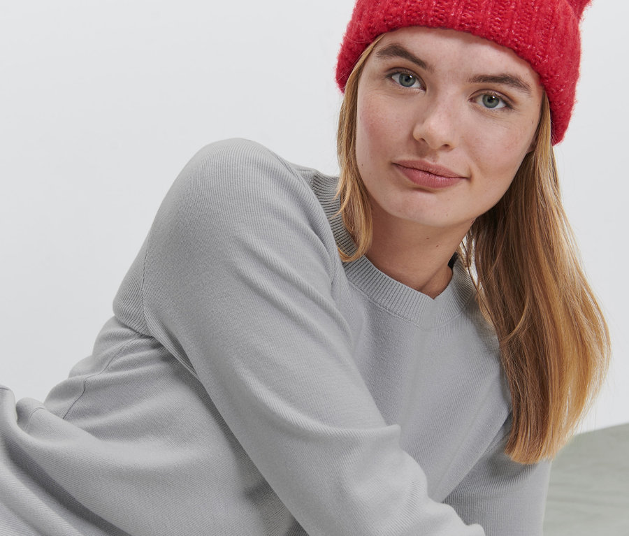 Frau liegt und trägt einen grauen Strickpullover und eine rote Mütze.