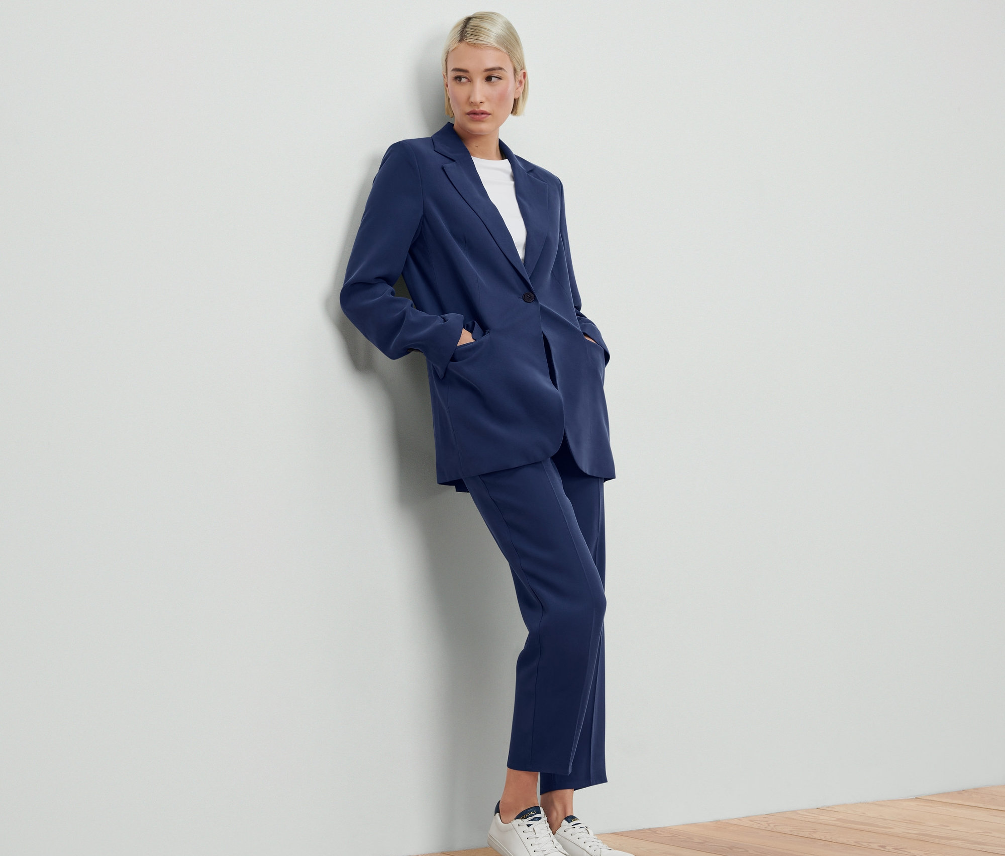 Frau lehnt an Wand und trägt blauen Webblazer mit passender Hose.