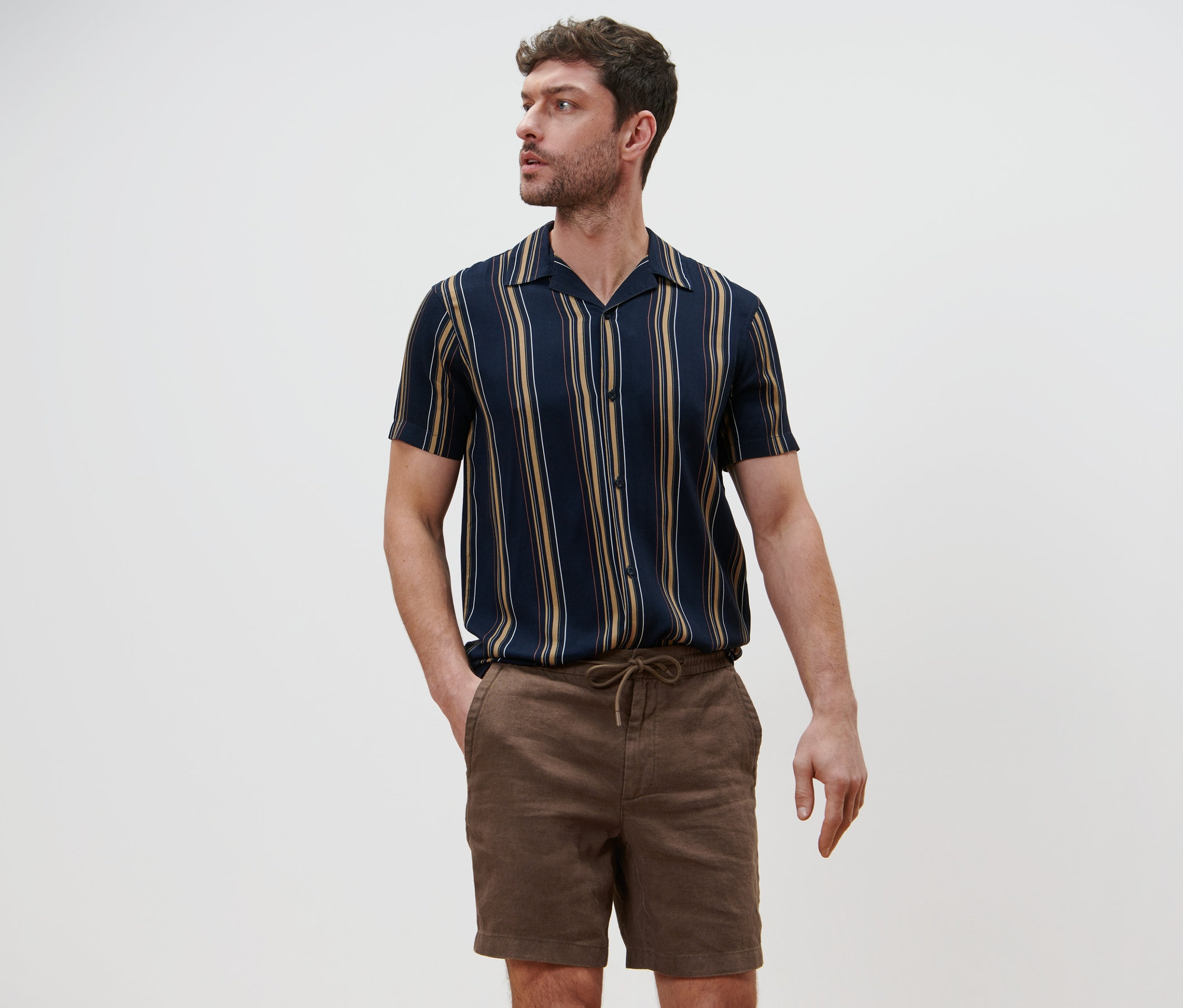 Mann posiert in Leinen-Shorts und gestreiftem Hemd.