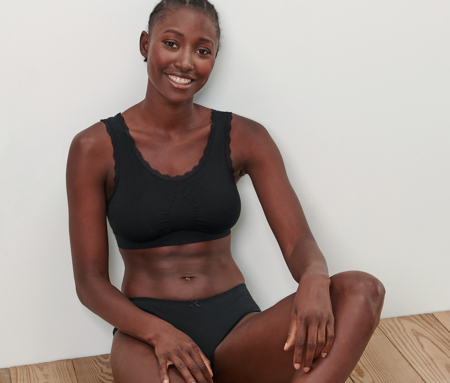 Frau sitzt auf Holzboden und trägt ein schwarzes Seamless-Bustier.
