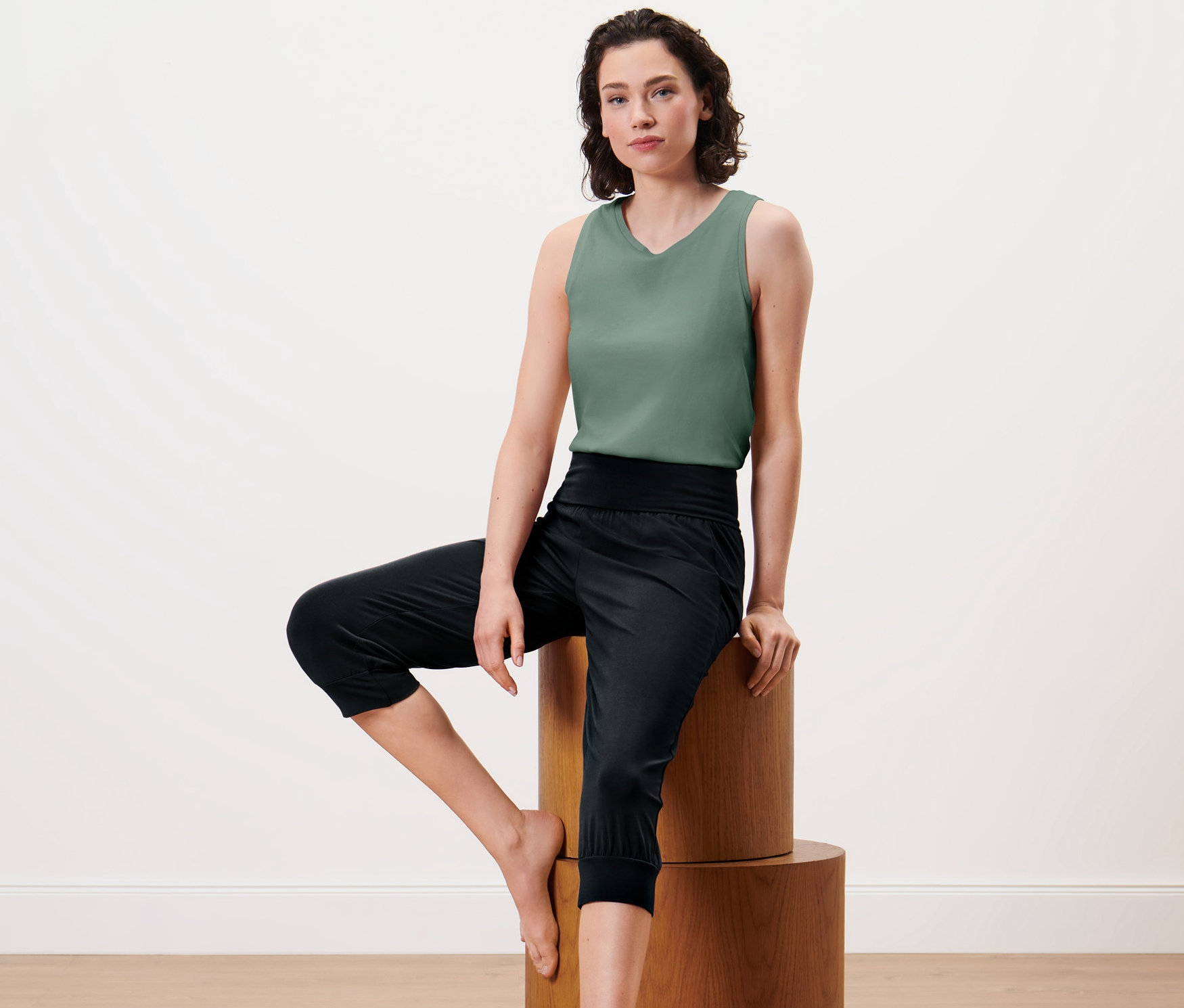 Frau sitzt auf Holzsockel, trägt eine 3/4-Yogahose.