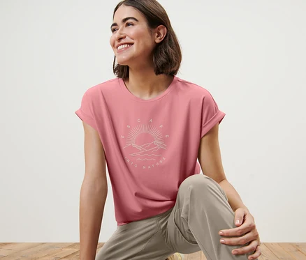 Frau auf Holzboden trägt ein rosafarbenes T-Shirt mit Print.