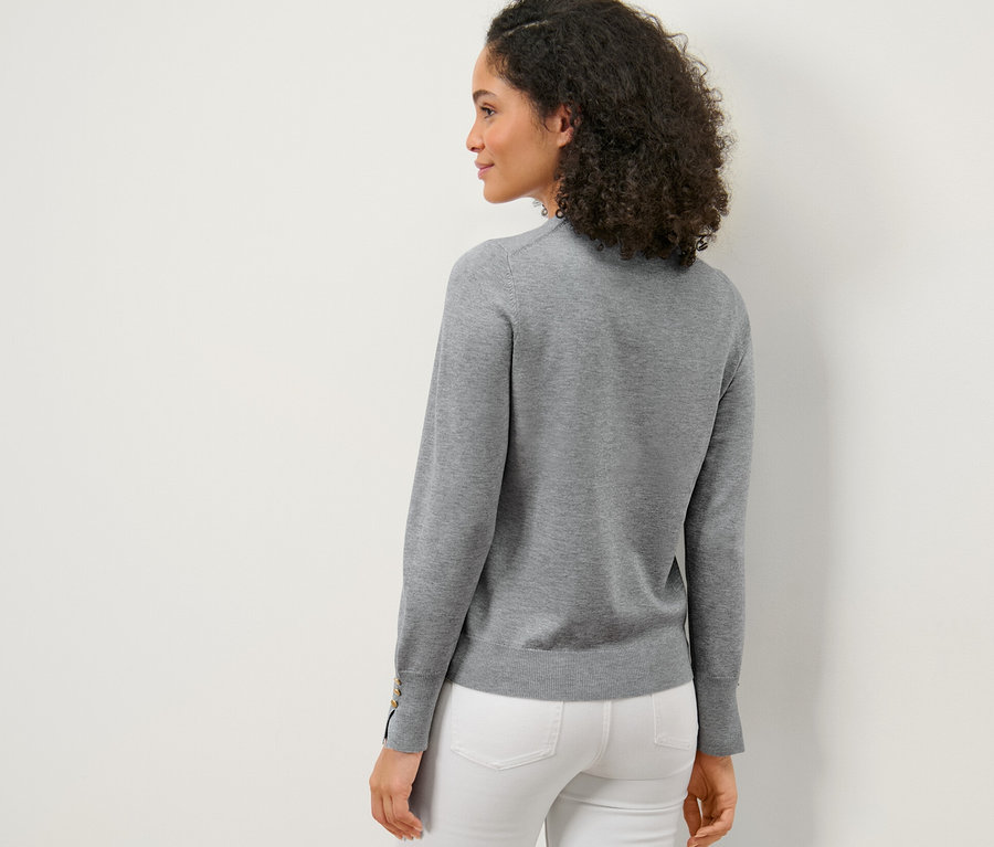 Frau posiert von hinten mit einem grau melierten Feinstrickpullover und weißen Hosen.