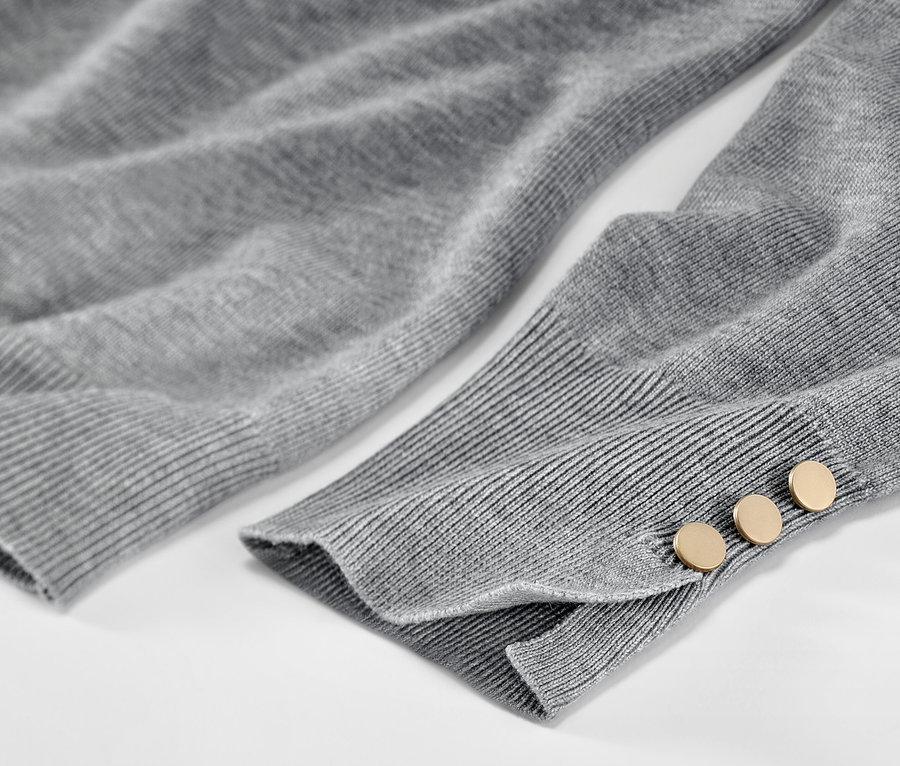 Detailaufnahme eines grau melierten Feinstrickpullovers mit Knöpfen am Ärmel.