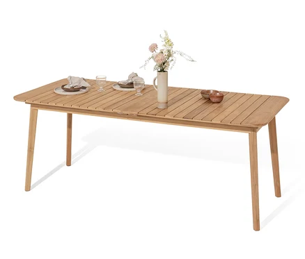 Ein doppelt ausziehbarer Teak-Tisch ist mit Tellern, Gläsern und Servietten gedeckt. In der Mitte des Tisches steht eine Vase mit Blumen.