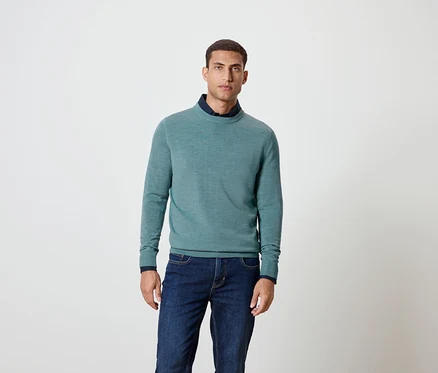 Mann posiert in blauem Pullover und Jeans.