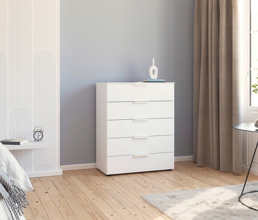 Weisse Kommode mit fünf Schubladen steht im Schlafzimmer neben Bett und Fenster.