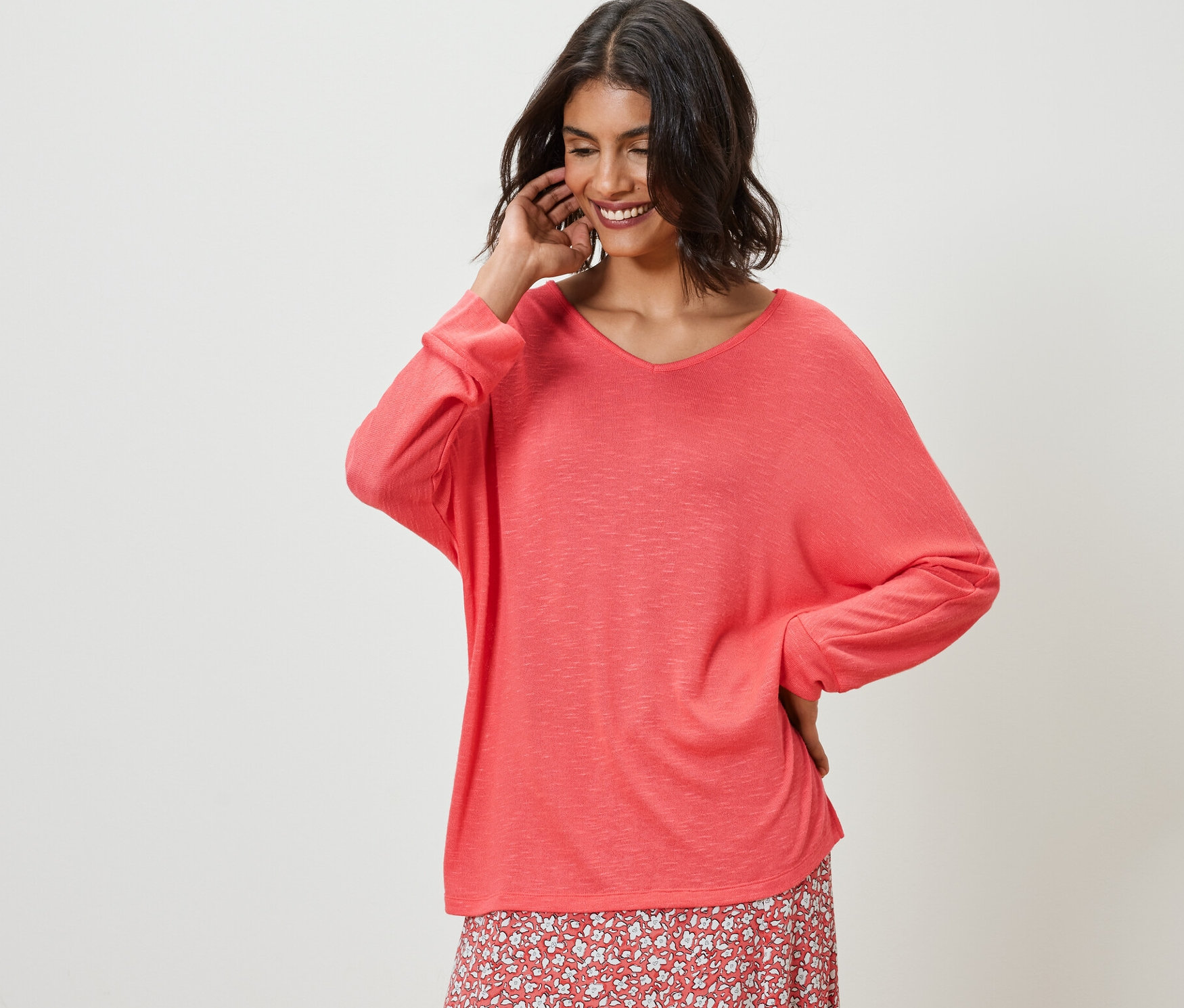 Frau posiert in korallefarbenem Fledermausshirt und Blumenrock.