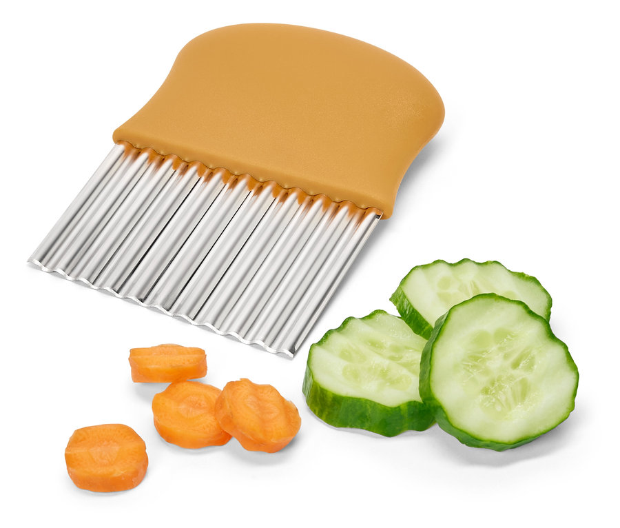 Wellenschneider mit orangefarbenem Griff neben geschnittener Gurke und Karotten.