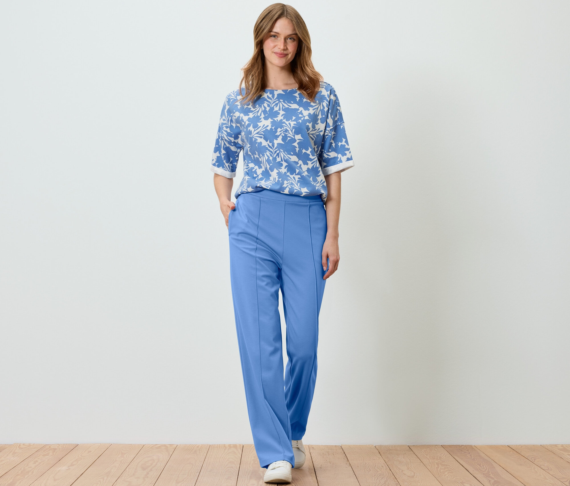 Frau posiert in hellblauem, bedrucktem Sweatshirt und blauer Hose.